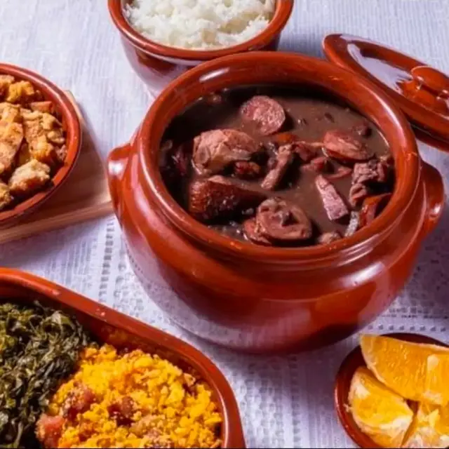 Feijoada completa servida em panela de barro com acompanhamentos